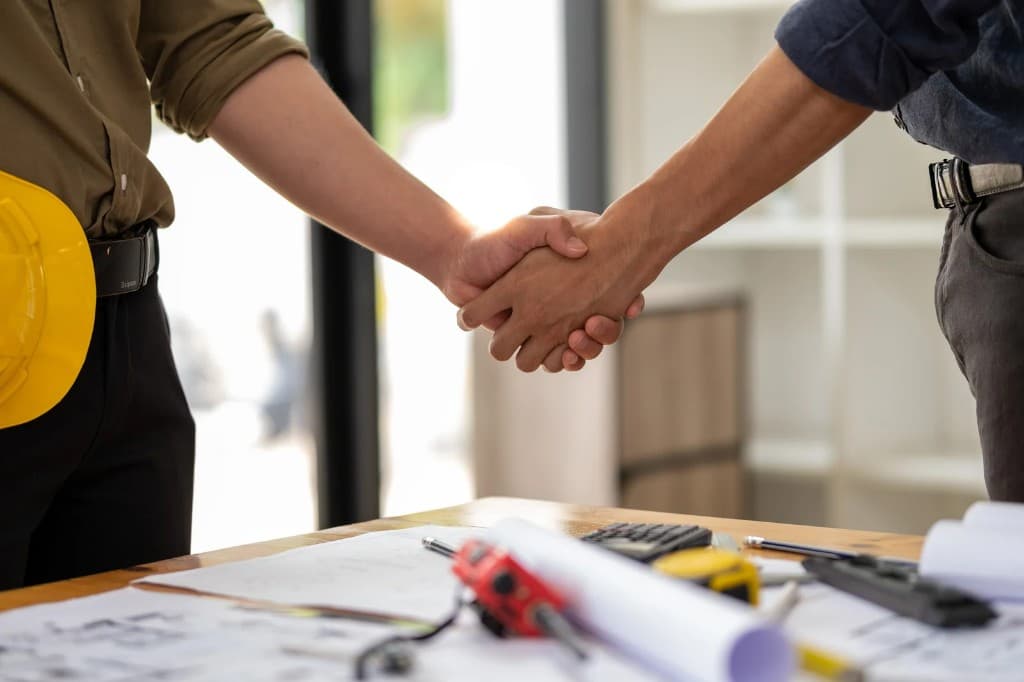 Two professionals shaking hands over construction plans