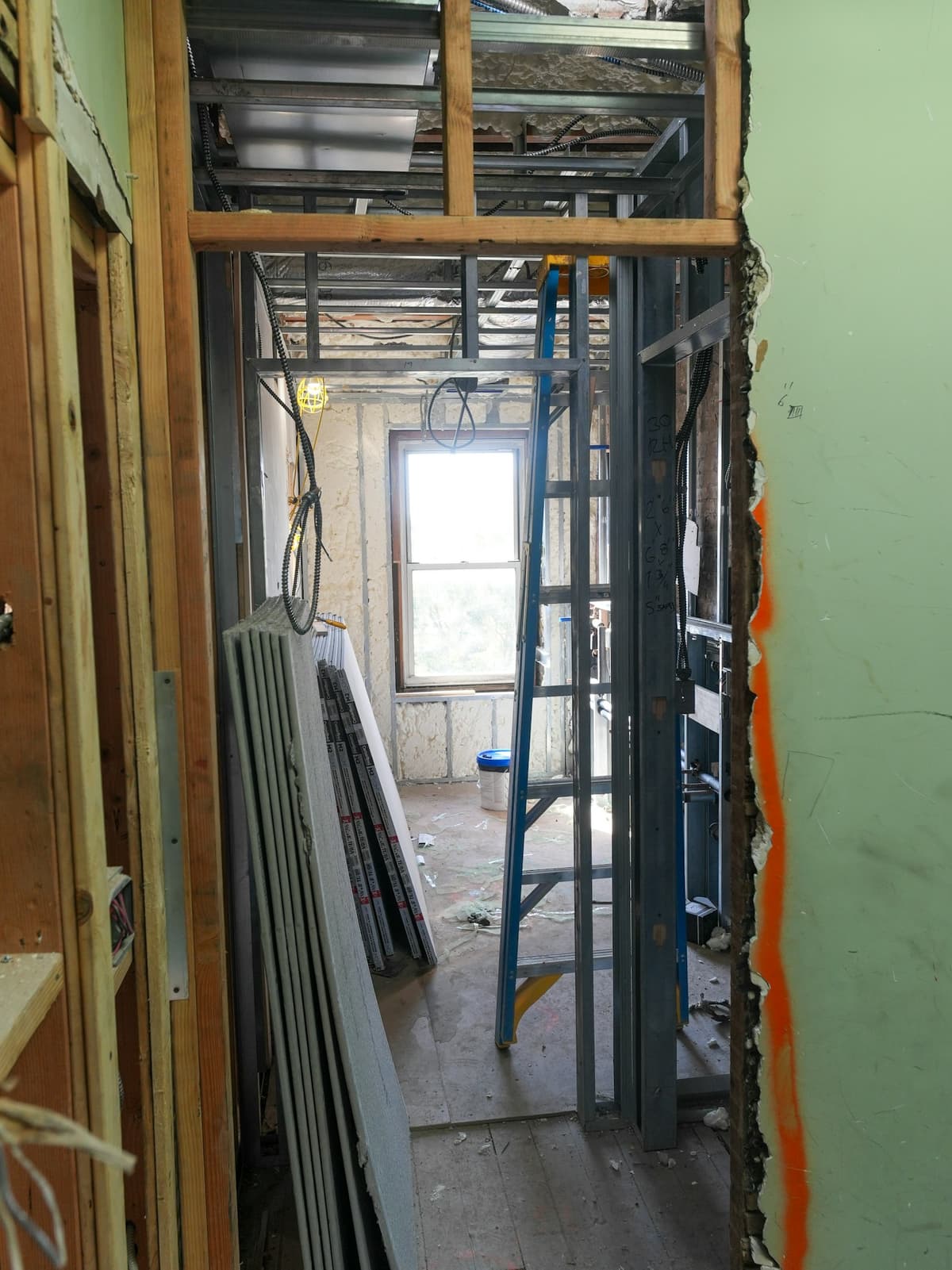 Framed interior renovation with stacked drywall sheets and a ladder